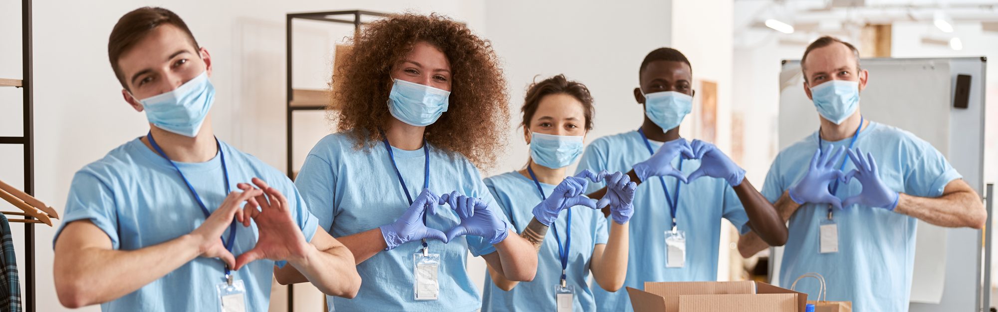 Equipo de voluntarios con uniformes celestes formando corazones con las manos